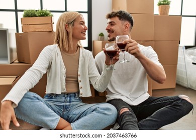 Young Caucasian Couple Toasting With Red Wine Glass Sitting At New Home.