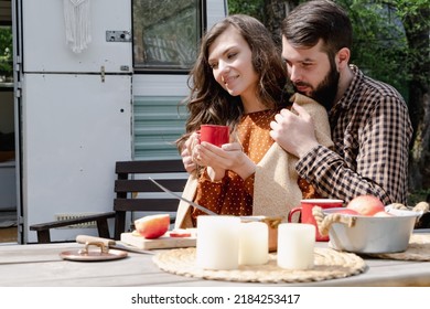 Young Caucasian Couple Is Traveling In Travel Van. Romantic Atmosphere Of Relaxation. Road Trip Around Country For The Weekend. Man And Woman Embrace Near Camper And Drinking Tea Or Mulled Wine