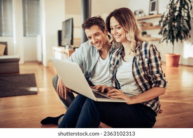 Young Caucasian couple using a laptop in the living room at home - Powered by Shutterstock