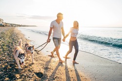 Young Caucasian Couple Walking On Beach With Siberian Husky Dogs