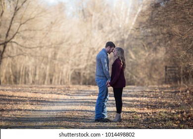 Young caucasian couple walking on dim gravel, dirt, rural, country road holding hands, kissing,smiling, laughing in love having fun season late winter bare trees - Powered by Shutterstock