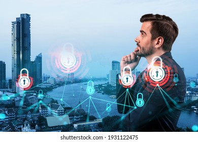 A young Caucasian cybersecurity developer thinking about new concepts at security compliance division to protect clients confidential information. IT lock icons over Bangkok background.