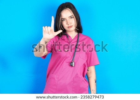 Young caucasian doctor woman wearing pink uniform making fun of people with fingers on forehead doing loser gesture mocking and insulting.