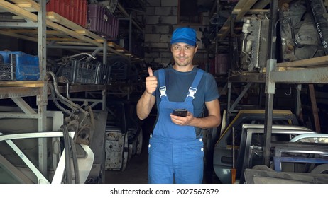 A Young Caucasian, An Employee Of A Car Disassembly, Completes Or Checks Car Spare Parts For A Client From A Tablet Computer At An Auto Parts Warehouse. A Man In A Blue Uniform.