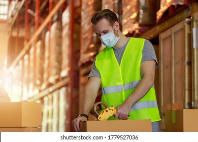 Young Caucasian Employee Male Packing Cardboard Box With Scotch Tape, Wearing Protective Face Mask, New Normal After Pandemic Crisis.