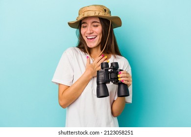 Young Caucasian Explorer Woman Holding Binoculars Isolated On Blue Background Laughs Out Loudly Keeping Hand On Chest.