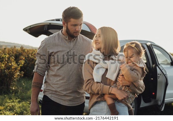 Young\
Caucasian Family Enjoying Road Trip, Mother and Father with Little\
Daughter Outdoors with SUV Car on\
Background