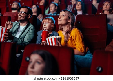 A young Caucasian family in in a movie theater watching a film together and having a good time.