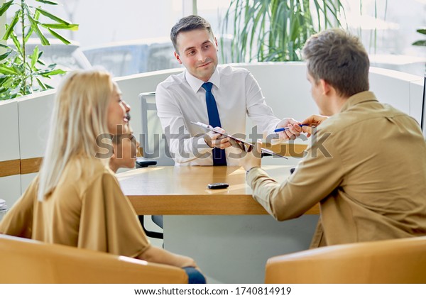young caucasian family read documents and talk with
consultant before purchase, they sit at table after view all cars
represented there
