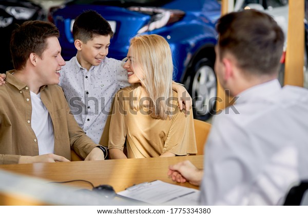 young caucasian family read documents and talk with\
consultant before purchase, they sit at table after view all cars\
represented there