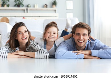 Young Caucasian Family With Small Daughter Pose Relax On Floor In Living Room, Smiling Little Girl Kid Hug Embrace Parents, Show Love And Gratitude, Rest At Home Together