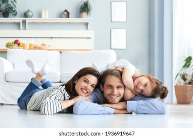 Junge kaukasische Familie mit kleiner Tochter entspannen sich auf dem Boden im Wohnzimmer, lächelnde kleine Mädchen Umarmung Eltern, zeigen Liebe und Dankbarkeit, ruhen Sie sich zusammen zu Hause