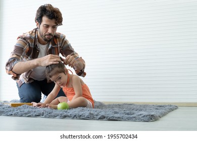 Young Caucasian Father With Beard Taking Care Of Little Adorable Child On Floor At Home. Dad Carefully Grab And Tied Up  Ponytail Hair To His Daughter