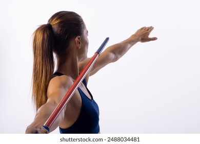 Young Caucasian female athlete practices javelin throwing technique indoors on a white background. Her focused stance suggests dedication to the sport of athletics. - Powered by Shutterstock