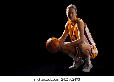 Young Caucasian female basketball player crouches in a basketball pose on a black background, with copy space. She's in a sports uniform, showcasing athleticism and focus on the court. - Powered by Shutterstock