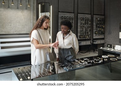 Young Caucasian female consumer choosing ring with help of African shop assistant while standing by large display - Powered by Shutterstock