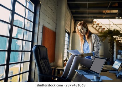 Young Caucasian female designer going over paperwork while working in a startup company office - Powered by Shutterstock