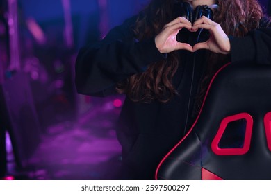 Young caucasian female gamer streamer creating heart gesture in gaming setup.