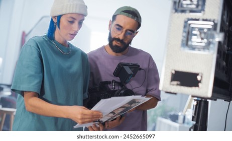 Young Caucasian Female And Middle Eastern Male Cinematographers Review A Script By A Camera On A Busy Film Set, Focusing On Video Production For A Documentary Or Tv Show.
