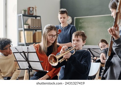 Young Caucasian female music teacher working with middle school orchestra helping boy to practice trumpet - Powered by Shutterstock