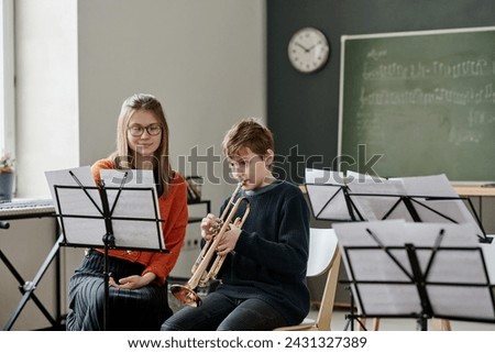 Young Caucasian female music teacher listening to middle school student playing trumpet during class