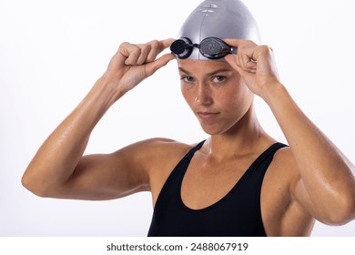 Young Caucasian female swimmer adjusts her swimming goggles on a white background. Captured in a studio, she's ready for a swim training session. - Powered by Shutterstock