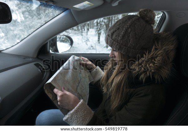 Young Caucasian female traveling by car in\
winter, looking for the right way on the\
map