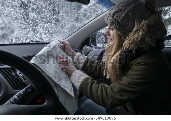 Young Caucasian female traveling by car in
winter, looking for the right way on the
map