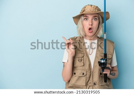 Young caucasian fisherwoman holding a rod isolated on blue background pointing to the side