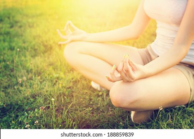 Young Caucasian fit and slim woman doing yoga outdoors in summer. Woman sitting in grass in yoga position with hands on her knees. Yoga lifestyle concept.