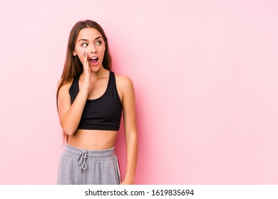 Young caucasian fitness woman posing in a pink background is saying a secret hot braking news and looking aside