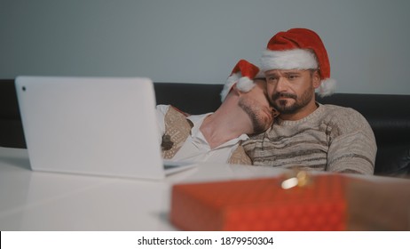 Young Caucasian Gay Couple With Santa Claus Hats Watching Movies On The Laptop On The Christmas Eve. High Quality Photo