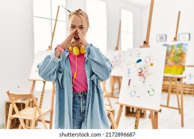 Young caucasian girl at art studio shouting angry out loud and hands over mouth 