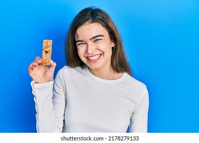 Young Caucasian Girl Eating Protein Bar As Healthy Energy Snack Looking Positive And Happy Standing And Smiling With A Confident Smile Showing Teeth 