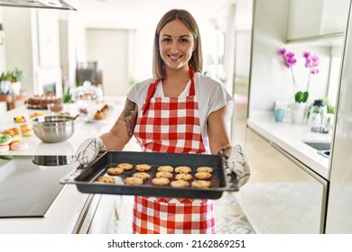 Young caucasian girl smiling happy holding tray with cookies at the kitchen.