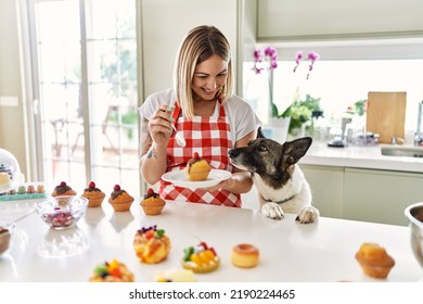 Young caucasian girl smiling happy with dog cooking pumpkins at the kitchen.