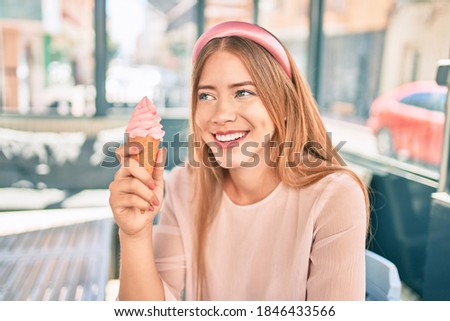 Young caucasian girl smiling happy eating ice cream sitting at coffee shop terrace.