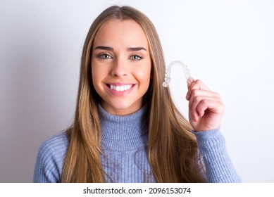 Young caucasian girl wearing blue turtleneck over white background holding an invisible braces aligner recommending this new treatment. Dental healthcare concept.