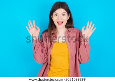Young caucasian girl wearing casual clothes isolated over blue background raising hands up, having eyes full of happiness rejoicing his great achievements. Achievement, success concept.