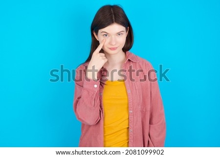 Young caucasian girl wearing casual clothes isolated over blue background , looking, observing, keeping an eye on an object in front, or watching out for something.