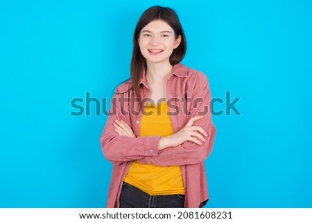 Young caucasian girl wearing casual clothes isolated over blue background being happy smiling and crossed arms looking confident at the camera. Positive and confident person.