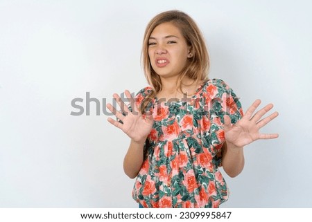 young caucasian girl wearing floral dress over white background afraid and terrified with fear expression stop gesture with hands, shouting in shock. Panic concept.