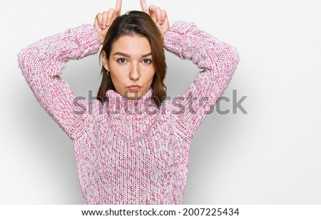 Young caucasian girl wearing wool winter sweater doing funny gesture with finger over head as bull horns 