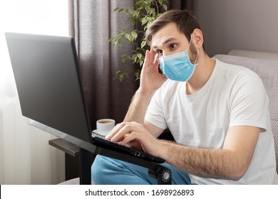 Young Caucasian Gloomy Man In Stress Working From Home Office Wearing Protective Mask Using Laptop And Internet. Coronavirus Covid 19 Quarantine. Remote Work, Freelancer, Home Office Workplace On Sofa