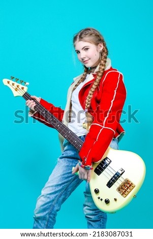 Young Caucasian Guitar Player With Yellow Bass Guitar Posing In Fashionable Red Jacket Over Trendy Turquoise Background. Vertical Shot