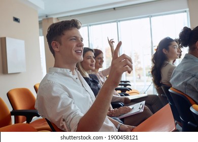 young  caucasian guy at business seminar raising hand, smiling