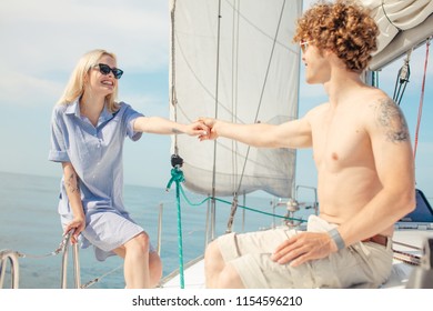 Young caucasian guy and girl in love travelling on board of a white yacht with sail set goes along the island on a hot sunny day. blue sea, blue sky, beautiful seaviews for wedding boat trip