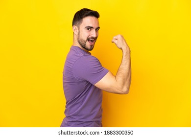 Young caucasian handsome man isolated on yellow background doing strong gesture - Shutterstock ID 1883300350