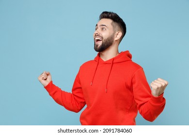 Young caucasian happy bearded excited overjoyed man 20s wearing casual red orange hoodie do winner gesture clench fist celebrating isolated on blue background studio portrait People lifestyle concept - Powered by Shutterstock