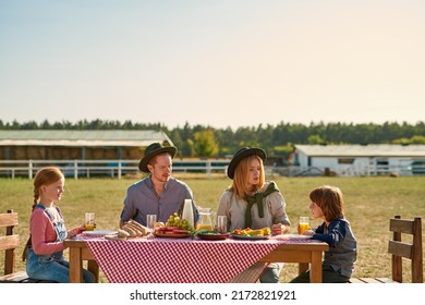 Young Caucasian Hipster Farm Family Having Lunch With Fresh Organic Products In Countryside Outdoors. Mother, Dad And Daughter Looking At Son. Children Drinking Juice. Modern Farm Lifestyle. Sunny Day